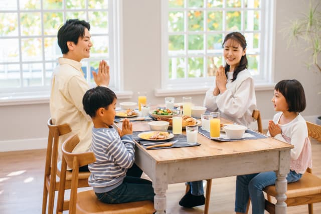 家族4人の食卓。食事前に4人で手を合わせている画像です。