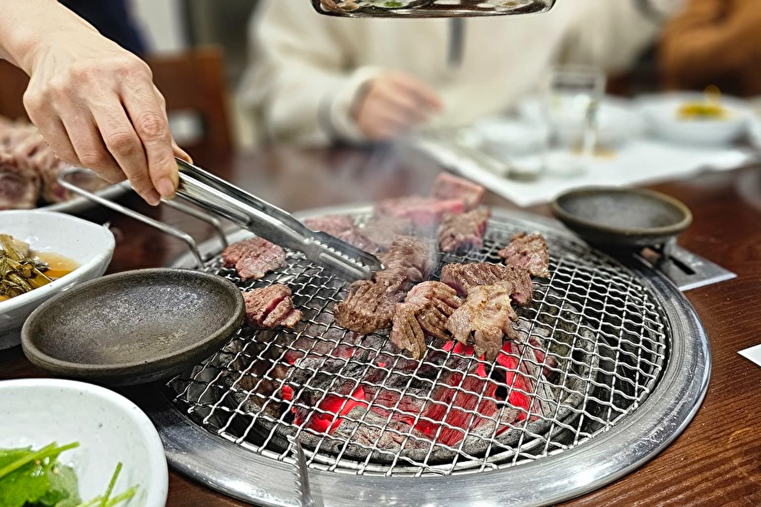 韓国の食事風景。炭火で焼き肉。トングをつかって肉をひっくり返している。